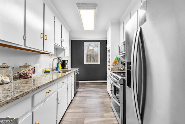 kitchen with white cabinets, sink, ornamental molding, appliances with stainless steel finishes, and light hardwood / wood-style floors