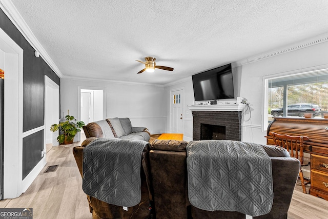 living room with a brick fireplace, ornamental molding, a textured ceiling, ceiling fan, and light hardwood / wood-style floors