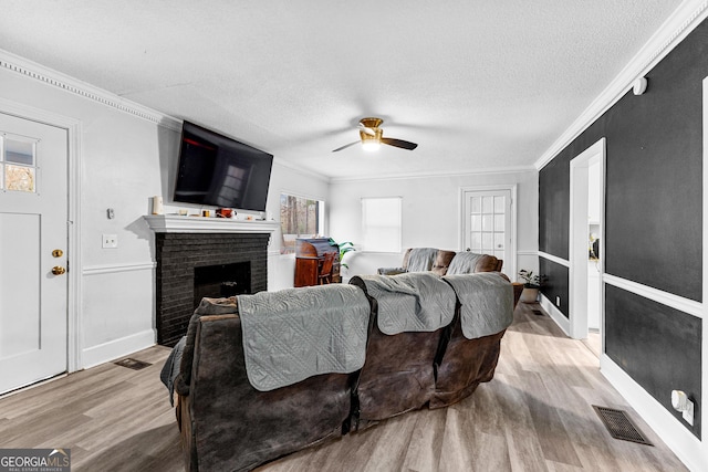 living room featuring a brick fireplace, crown molding, ceiling fan, and light wood-type flooring