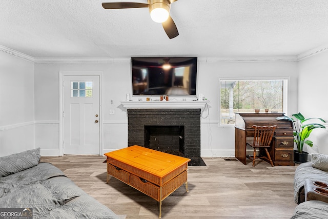 living room with crown molding, a brick fireplace, light hardwood / wood-style flooring, ceiling fan, and a textured ceiling