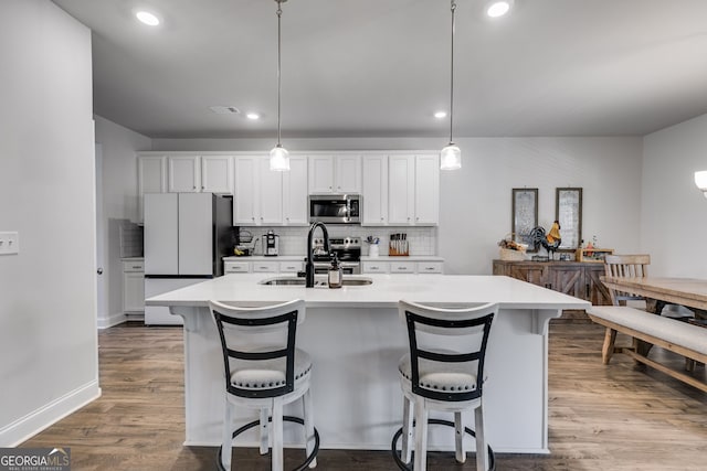 kitchen with pendant lighting, a kitchen island with sink, white cabinets, sink, and appliances with stainless steel finishes