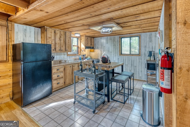 kitchen with black refrigerator, light tile patterned floors, wooden ceiling, and wood walls