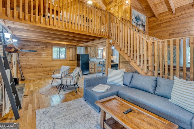 living room with beamed ceiling, light wood-type flooring, and wood walls