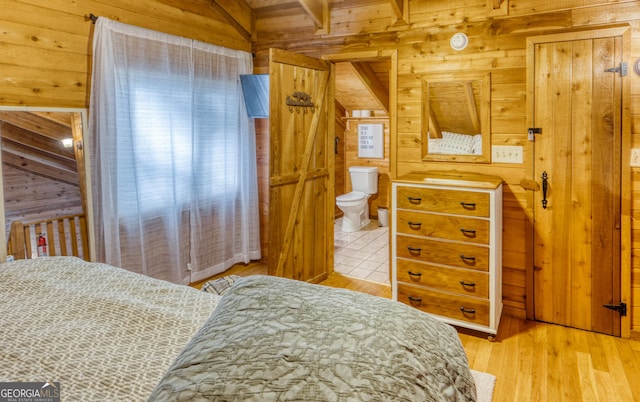 bedroom with ensuite bathroom, wood walls, and light wood-type flooring