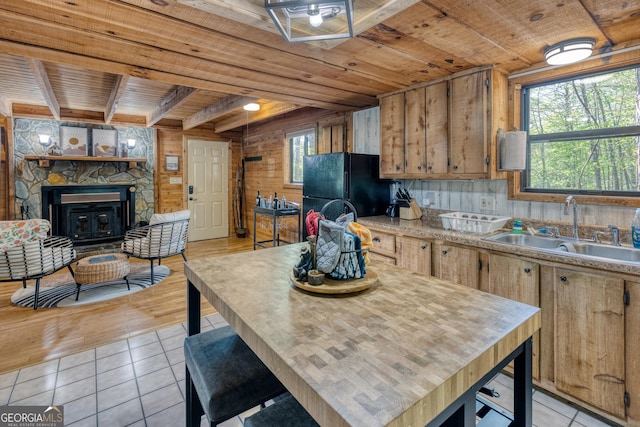 kitchen featuring wood walls, black fridge, a stone fireplace, sink, and light tile patterned flooring