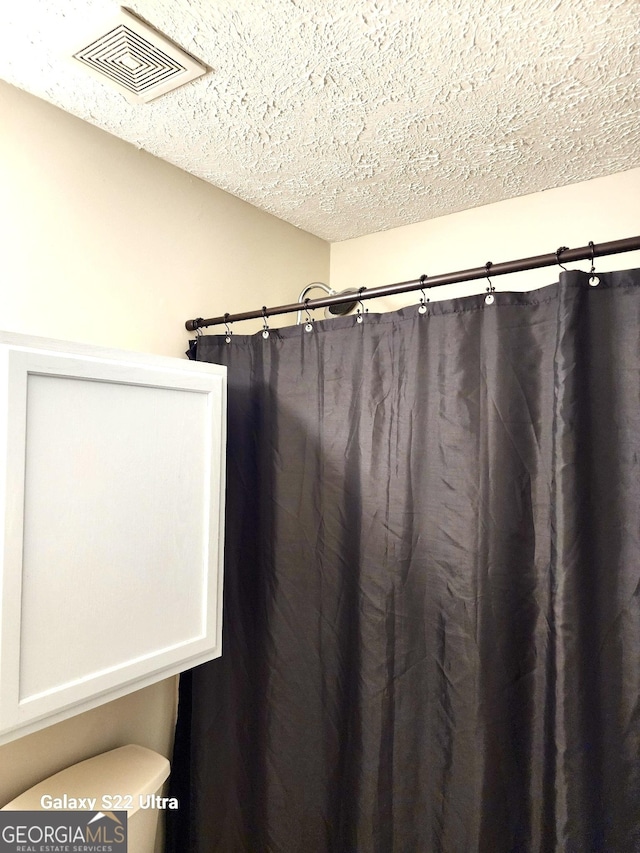 bathroom featuring curtained shower, a textured ceiling, and toilet