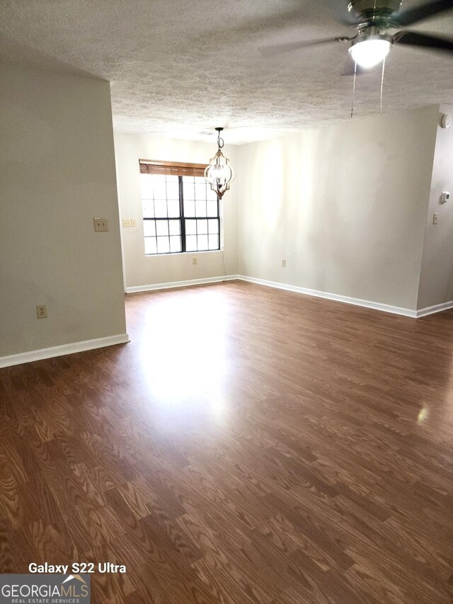 empty room featuring ceiling fan with notable chandelier, a textured ceiling, and dark hardwood / wood-style flooring