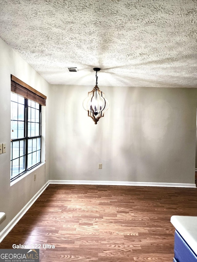 unfurnished dining area with wood-type flooring, a textured ceiling, and a notable chandelier