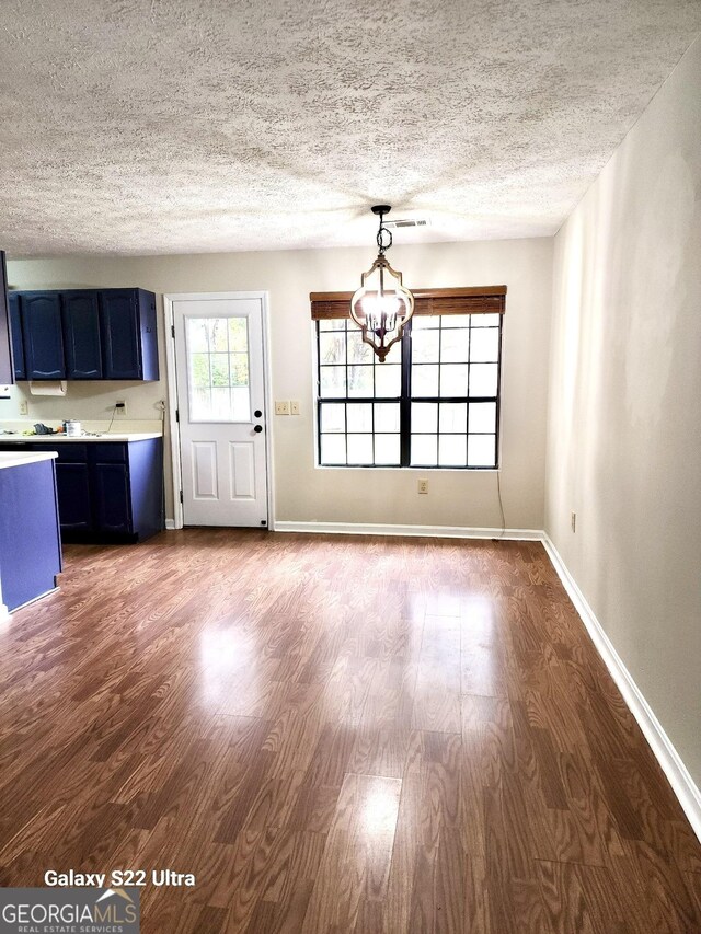 unfurnished living room with a notable chandelier, dark hardwood / wood-style flooring, and a textured ceiling