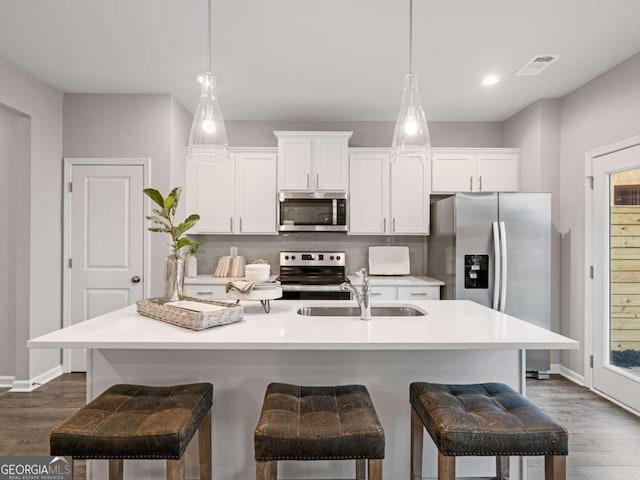 kitchen with dark hardwood / wood-style floors, sink, appliances with stainless steel finishes, and an island with sink