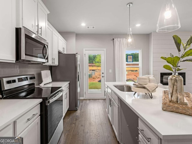 kitchen with white cabinetry, a large fireplace, sink, dark wood-type flooring, and stainless steel appliances