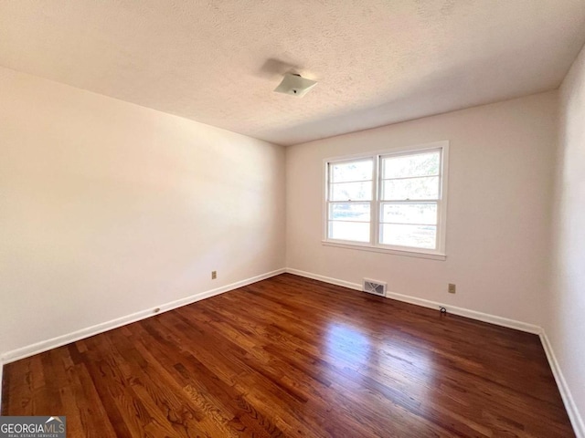 empty room with dark wood-type flooring and a textured ceiling