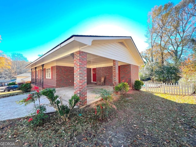 view of property exterior with a carport, fence, concrete driveway, and brick siding