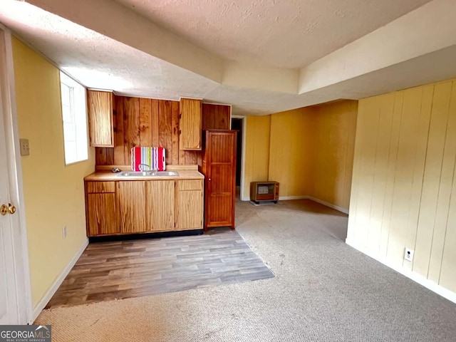 kitchen with wood walls, sink, a textured ceiling, and light wood-type flooring