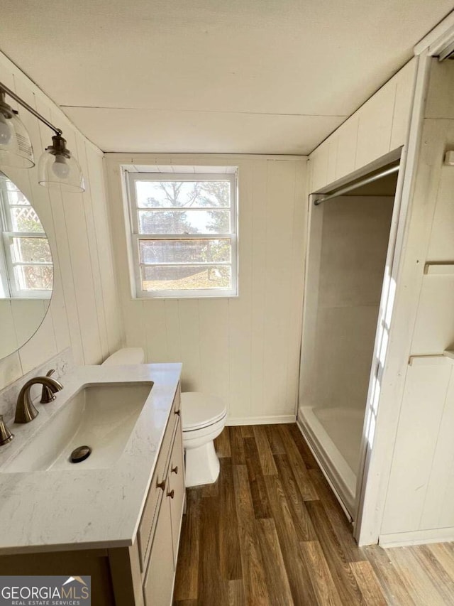 bathroom featuring walk in shower, vanity, wood-type flooring, toilet, and wood walls