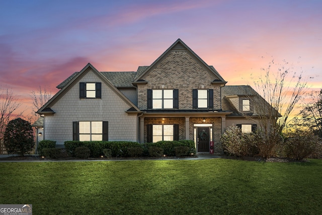 view of front of property featuring a shingled roof, brick siding, and a front lawn