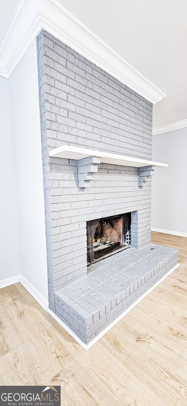 details with crown molding, wood-type flooring, and a brick fireplace