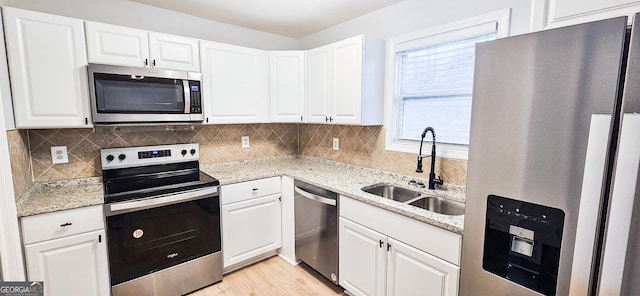 kitchen with white cabinets, appliances with stainless steel finishes, light stone counters, and sink