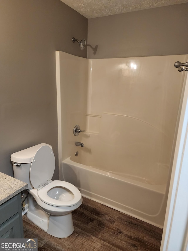 full bathroom with hardwood / wood-style floors, vanity, bathtub / shower combination, toilet, and a textured ceiling