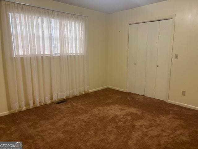 unfurnished bedroom with dark colored carpet and a closet