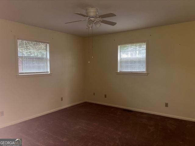 spare room with dark colored carpet, plenty of natural light, and ceiling fan