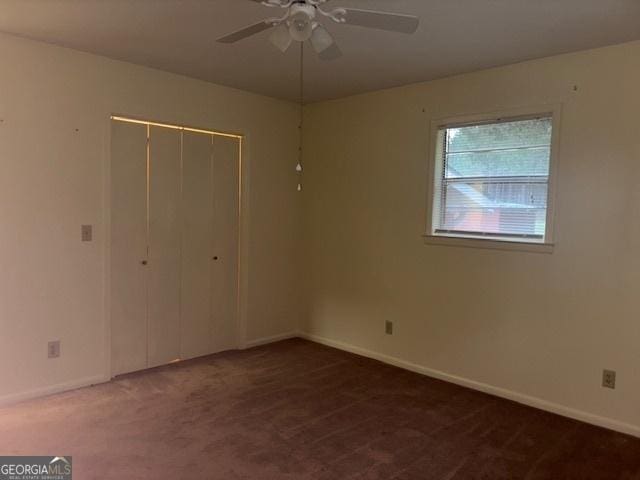 unfurnished bedroom featuring ceiling fan, dark carpet, and a closet