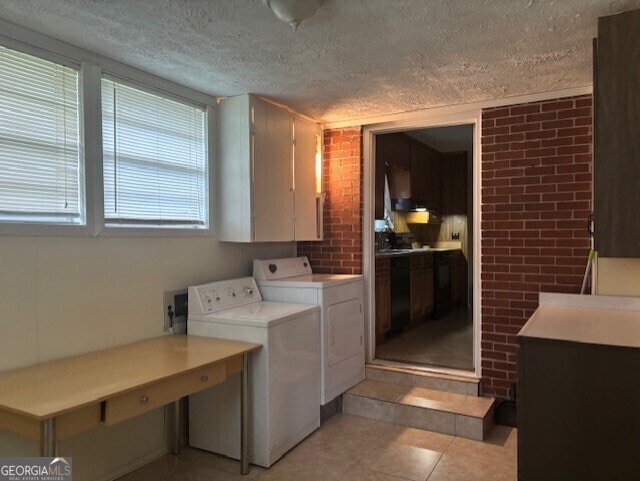 washroom with light tile patterned flooring, washing machine and dryer, a textured ceiling, and brick wall