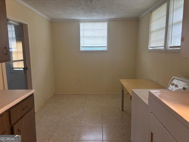 laundry room featuring cabinets, a textured ceiling, crown molding, washing machine and clothes dryer, and light tile patterned flooring