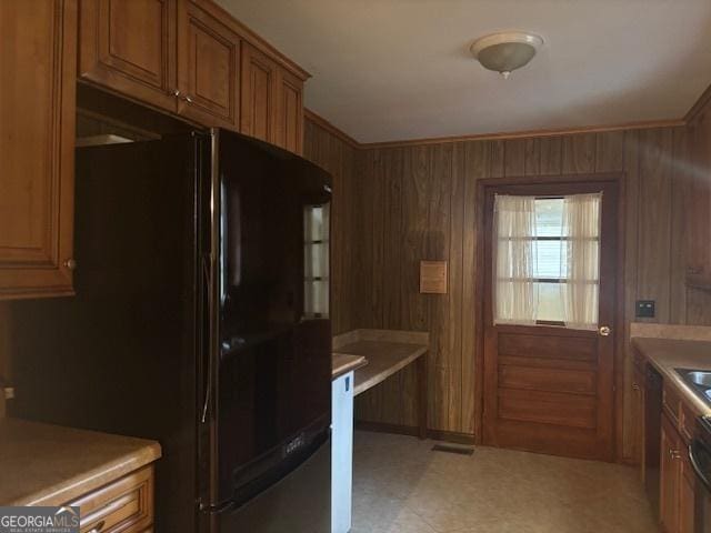 kitchen with black fridge, wood walls, and ornamental molding