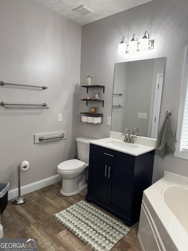 bathroom featuring hardwood / wood-style floors, vanity, toilet, a tub to relax in, and a textured ceiling