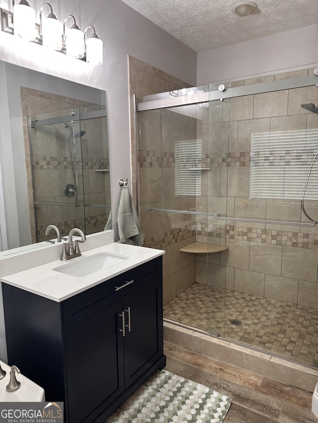 bathroom with vanity, a shower with shower door, and a textured ceiling