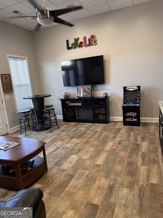 living room with wood-type flooring, a drop ceiling, and ceiling fan