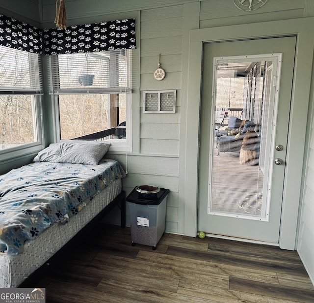 bedroom featuring multiple windows, dark wood-type flooring, and wood walls