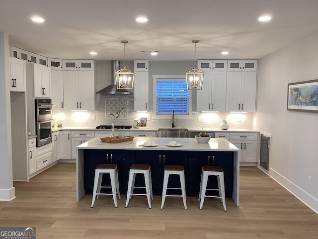 kitchen featuring white cabinetry, a center island, sink, and wall chimney range hood