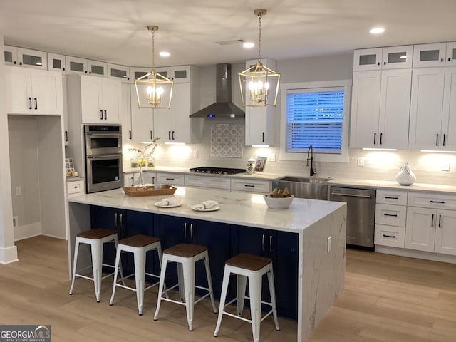 kitchen with sink, hanging light fixtures, a center island, stainless steel appliances, and wall chimney exhaust hood