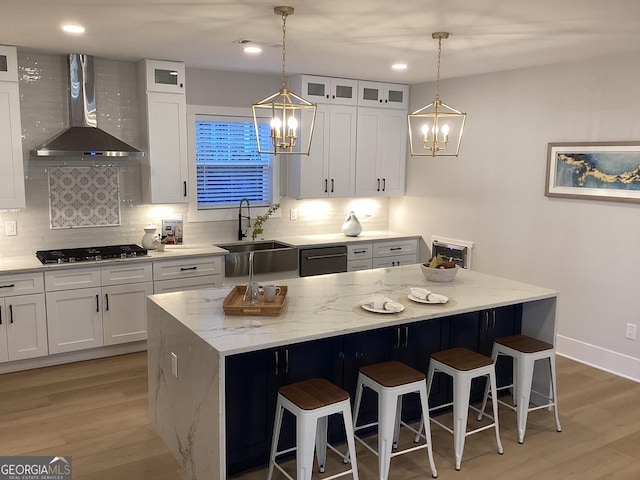 kitchen with white cabinetry, a kitchen island, sink, and wall chimney range hood