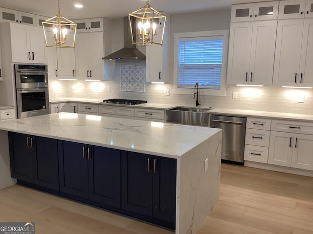 kitchen featuring sink, wall chimney range hood, a kitchen island, stainless steel appliances, and white cabinets