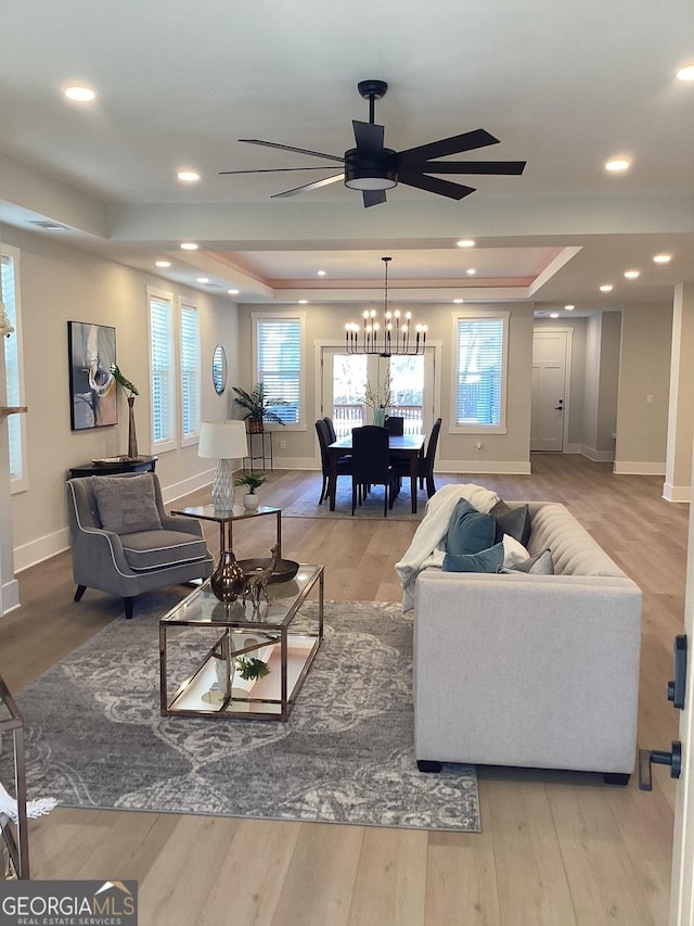 living room featuring a raised ceiling, ceiling fan, and light wood-type flooring