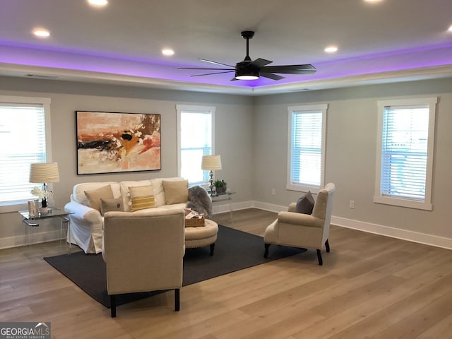 living area with hardwood / wood-style floors, a tray ceiling, and ceiling fan