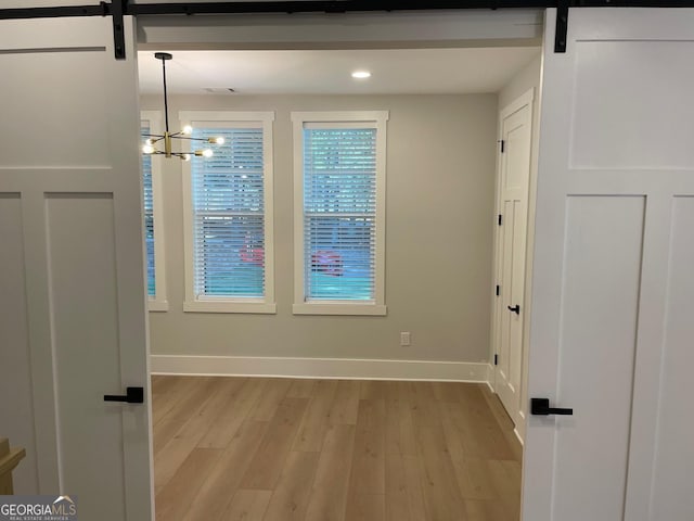 empty room with a barn door, a notable chandelier, and light wood-type flooring