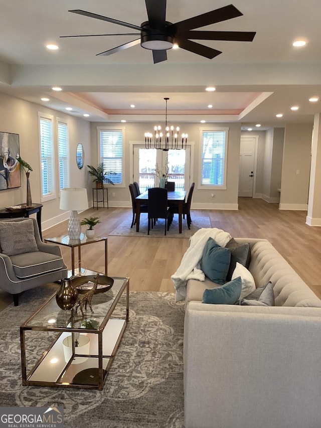 living room with a tray ceiling, plenty of natural light, light hardwood / wood-style floors, and ceiling fan with notable chandelier