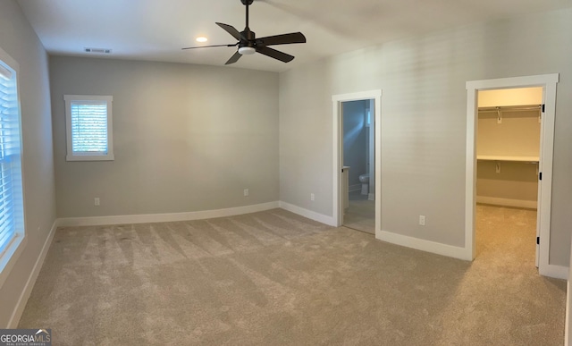 unfurnished bedroom featuring ceiling fan, connected bathroom, light carpet, a walk in closet, and a closet