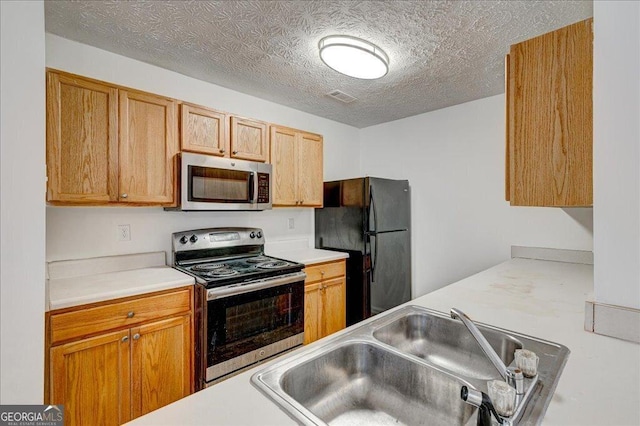 kitchen with appliances with stainless steel finishes, a textured ceiling, and sink