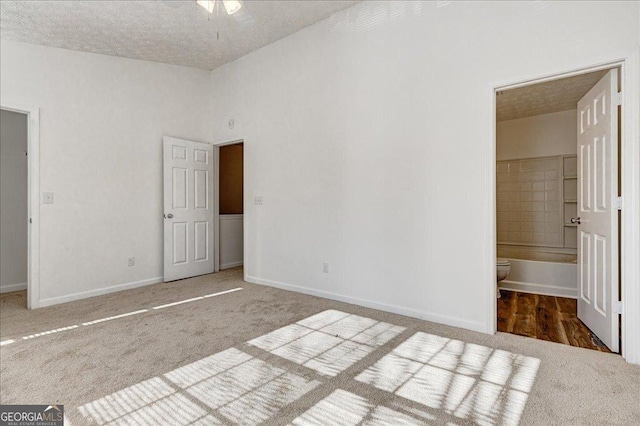 unfurnished bedroom with carpet flooring, ensuite bath, ceiling fan, and a textured ceiling