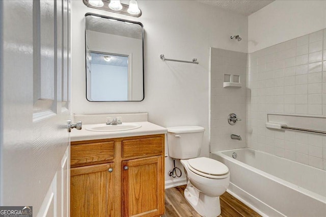 full bathroom featuring vanity, hardwood / wood-style flooring, tiled shower / bath combo, toilet, and a textured ceiling