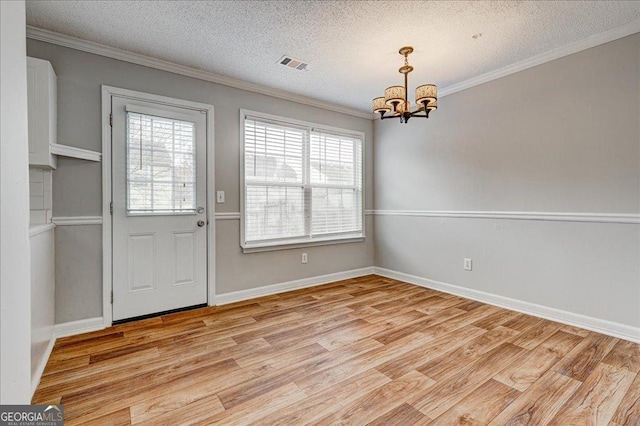 unfurnished dining area with light hardwood / wood-style floors, crown molding, a textured ceiling, and a chandelier