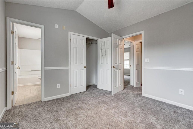 unfurnished bedroom featuring light carpet, a textured ceiling, vaulted ceiling, ceiling fan, and a closet