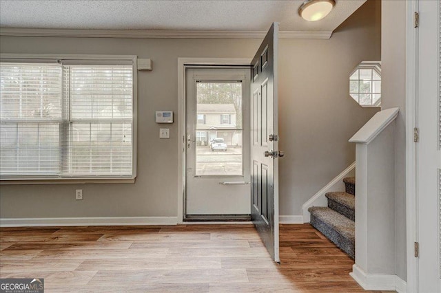 entryway with a textured ceiling, light wood-type flooring, and ornamental molding