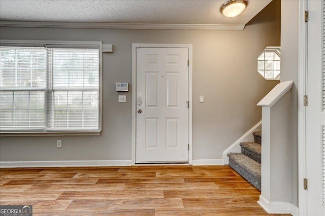 entryway featuring light wood-type flooring, a textured ceiling, and ornamental molding