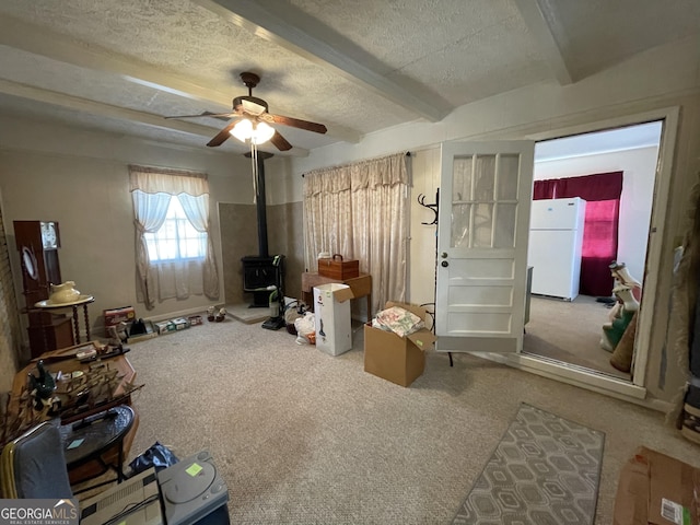 misc room with beam ceiling, a wood stove, ceiling fan, a textured ceiling, and carpet